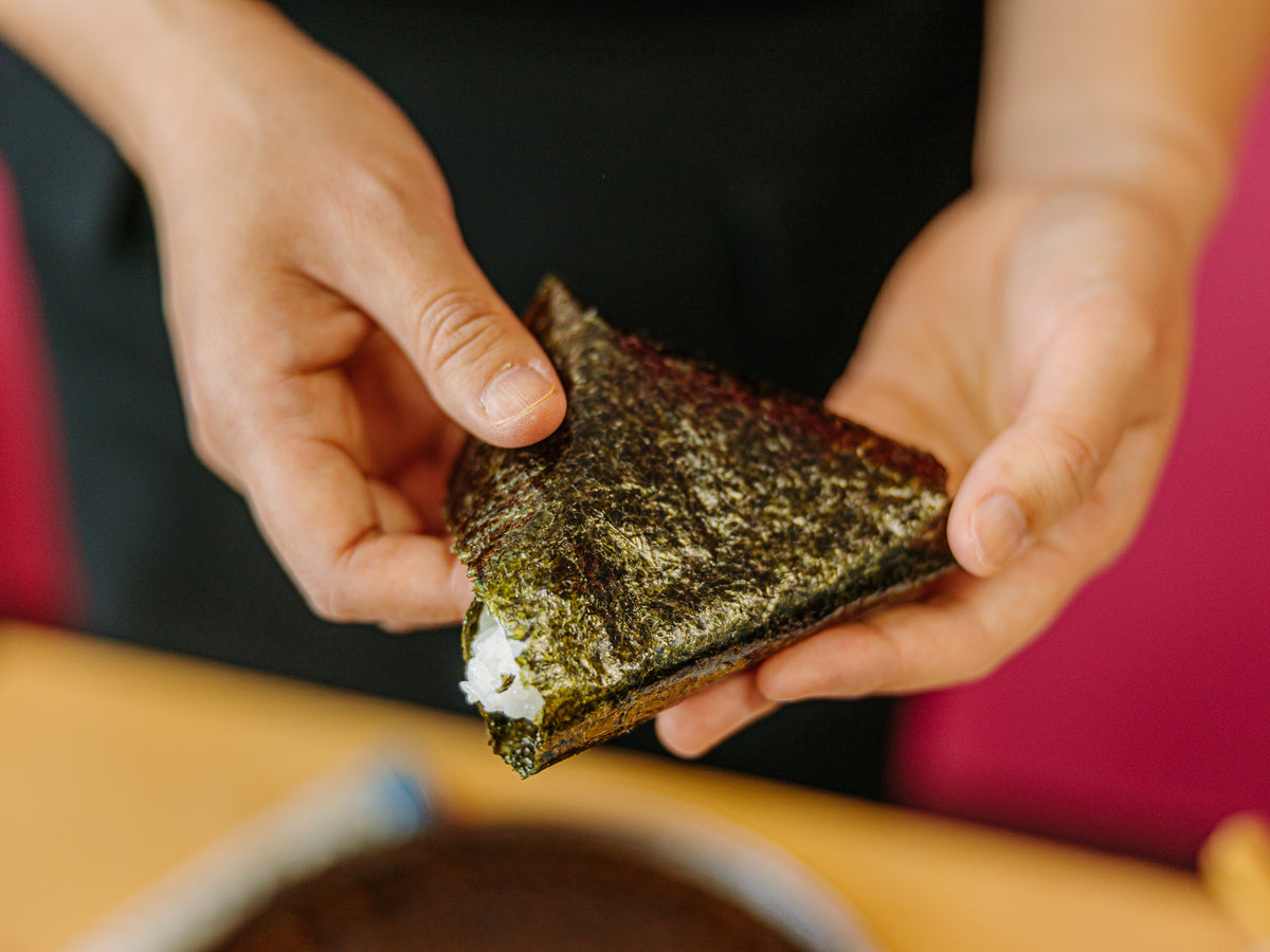 Hands holding fully unwrapped Japanese onigiri with nori seaweed – Bento&co