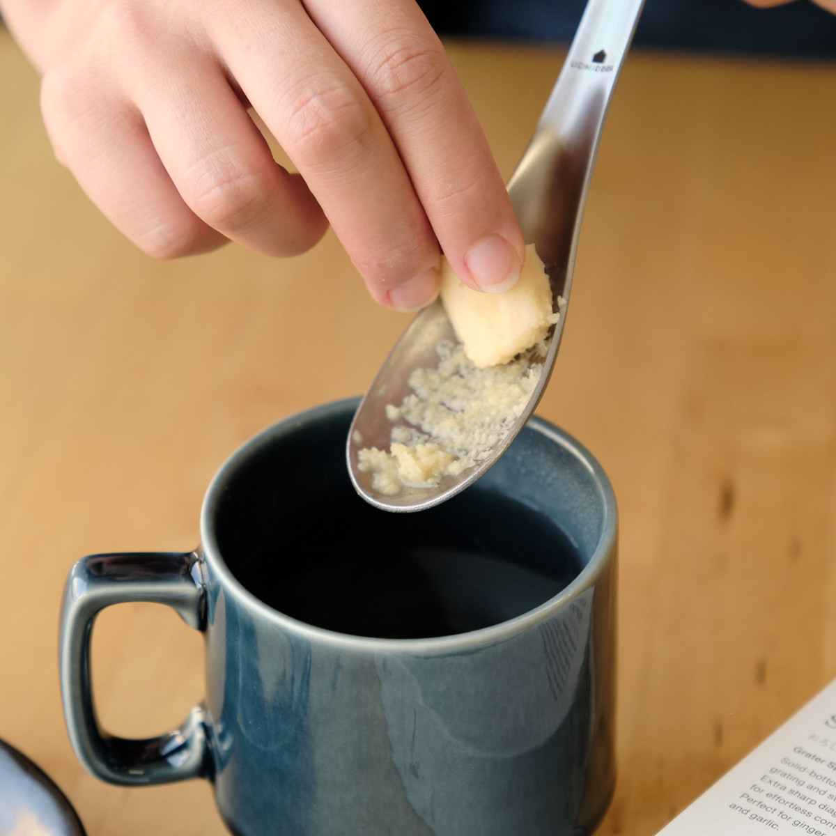 Close-up of Oroshi Grater Spoon grating fresh ginger into a ceramic mug