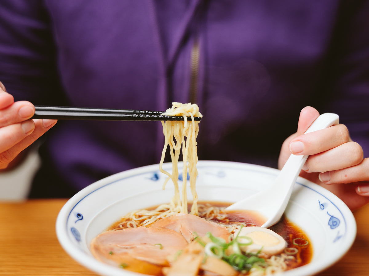 Person eating ramen with chopsticks and Porcelain Ramen Spoon – shoyu broth with chashu pork and green onions