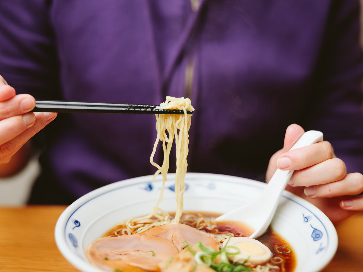 Tornado Chopsticks lifting ramen noodles from a shoyu ramen bowl with chashu pork and soft-boiled egg