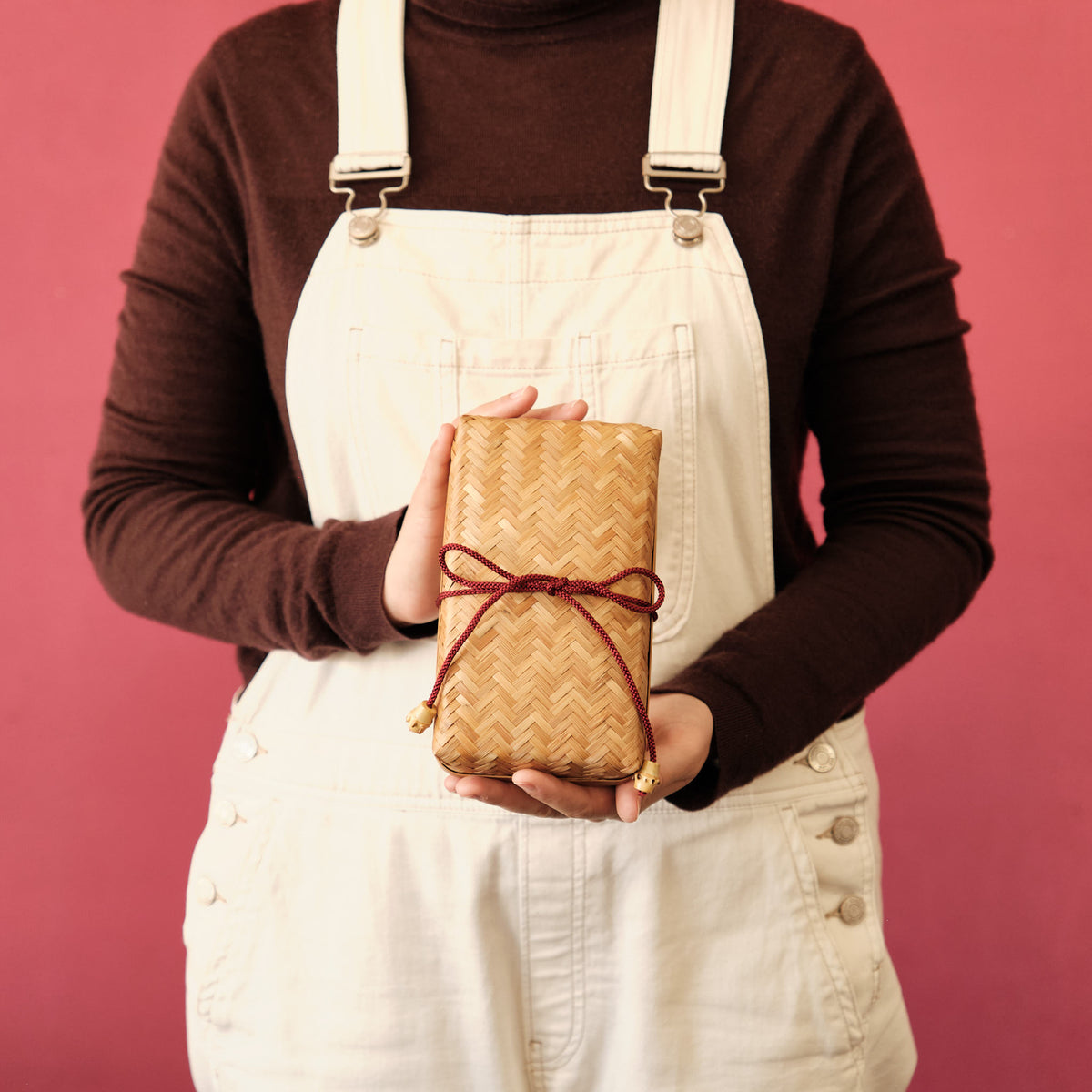 Person holding Woven Bamboo Bento Box with red braided cord on pink background, showing size reference